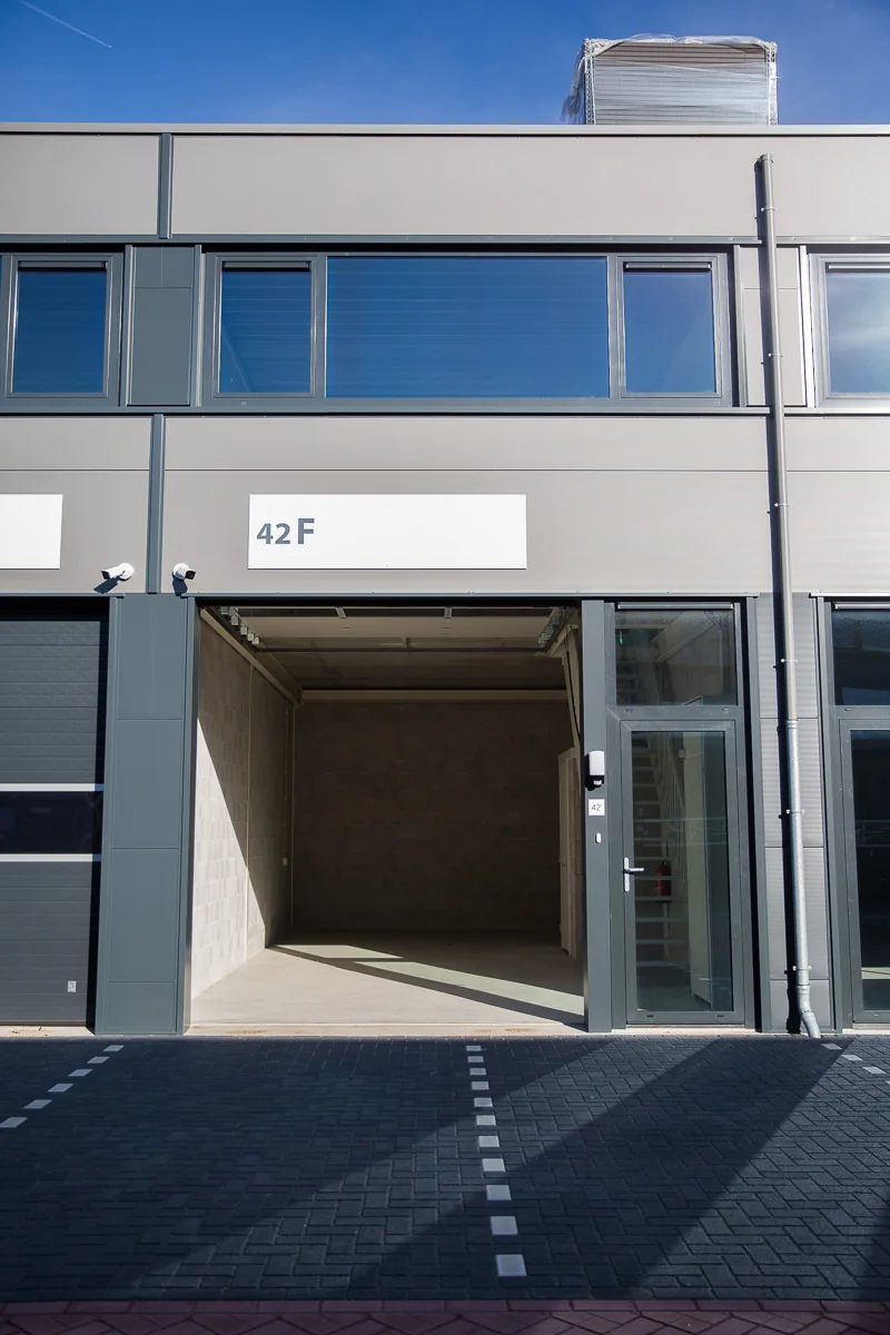 Grijze bedrijfsunit met open garagepoort en glazen deur op de Laan van 's-Gravenmade, unitnummer 42F.